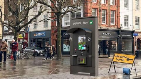 An artist impression of a JCDecaux Communication Hub in St Sampson's Square, York. The hub is about 10 ft in height and the word Defibrillator is visible on the front. There is also a digital screen in the middle.