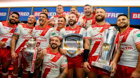 Hull KR players hold their three trophies and their winners rings in a posed photo in the dressing room after their Grand Final triumph over Wigan Warriors.