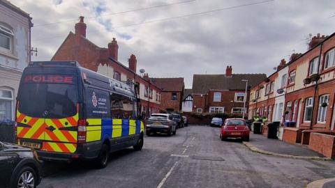 A large dark blue liveried police transit van parked amongst cars on the left hand side of Tyne Avenue, a terraced street in Blackpool.