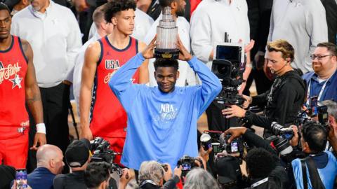 Anthony Edwards holds the All-Star MVP trophy above his head as photographers take his picture 