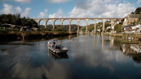 Passengers on the new ferry with the Calstock Viaduct behind them. The sky is blue and cloudy. 