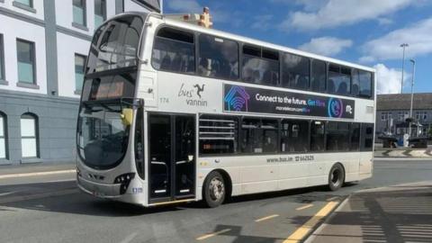 A silver double-decker bus, with a digital screen, drives away from the roundabout at the Sea Terminal.