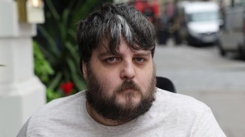 Nathan Rollinson, a man with brown and grey hair and a beard in a light t-shirt