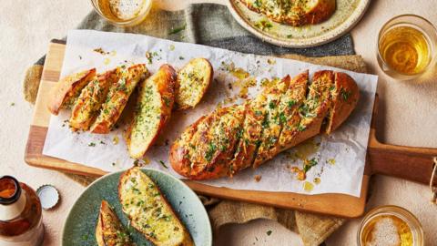 A wooden chopping board with a loaf of garlic bread.