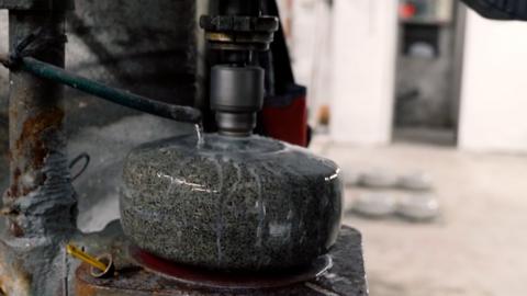 Curling stone on a machine being ground, with water running down the side.