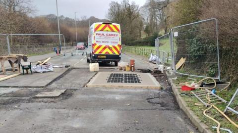 Roadworks including freshly laid concrete and a metal rectangular grid.