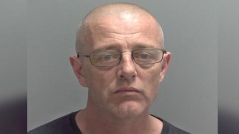 A police mugshot of Timothy Neale looking straight at the camera, he is wearing a dark top and wearing glasses