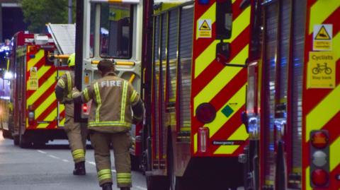 A firefighter stepping out of a fire engine parked by the side of a road.