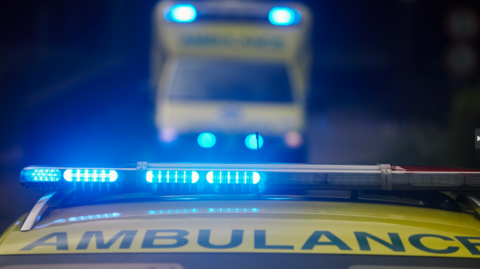 The blue lights of an ambulance shine in the foreground of the image with a blurred view of another ambulance behind it