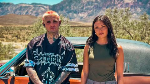 Tir Dhondy stands next to a man and car in the desert in Las Vegas. 