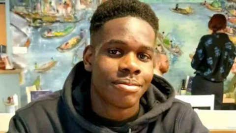 Boy smiling softly indoors while wearing a black hoodie