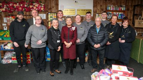 Michael Dunn, with Sue Snowdon, Lord Lieutenant for County Durham; Councillor Alan Shield, Durham County Council’s Cabinet member for equality and inclusion; Michael Laing, the council’s head of adult and health services; and members of the Angels Trust Team. They are in the hub surrounded by essentials such as tins of food and cleaning products.