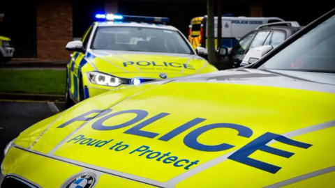 Two police cars fill the photo. They have lime green colouring and the words "Police Proud to Protect" written on the sides. 