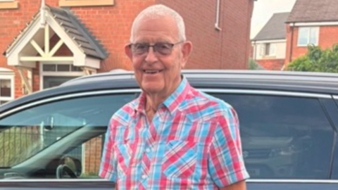 A man in a colourful shirt in front of a car