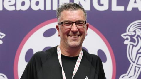 Richard Love, a man who is looking at the camera and smiling. He is wearing a black sports top and has a medal round his neck. 