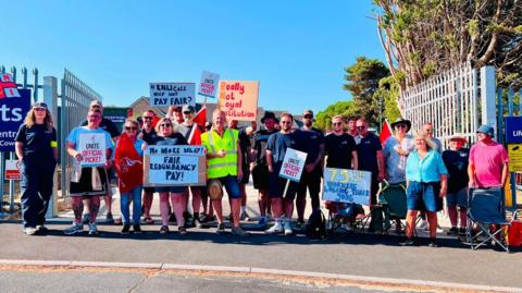 Strikers on a picket line outside the centre on a sunny day holding placards.