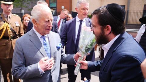 King Charles III is presented with flowers as he leaves the Jewish Care building during his visit to Golders Green