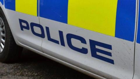 Close-up image shows police logo on police car. The car is white with the word 'police' written in blue.