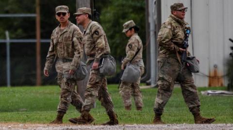 Four national guard troops from Texas are wearing camouflage uniforms and walking on grass