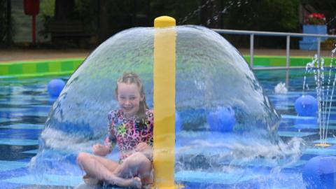 Young girl under splash park fountain