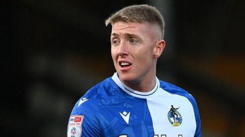 Joel Senior standing on the pitch wearing Bristol Rovers kit and looking over his right shoulder