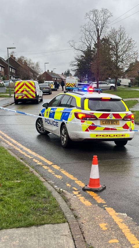 A police cordon with a marked car with its siren on.