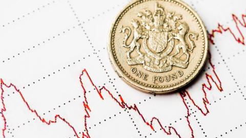 A one pound coin lies on a sheet with a wiggly red graphic line. 