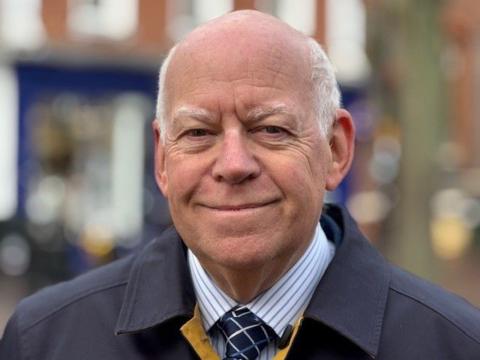 Dressed in a smart blue overcoat over a striped blue and white shirt and tie, West Berkshire Council leader Jeff Brooks is standing on the edge of Newbury's Market Place looking directly into the camera. 