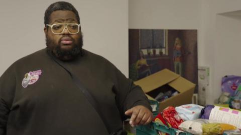 Solomon Smith leans one arm on a green crate of donated food.