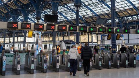 Two people walking through barriers at Brighton Railway Station.
