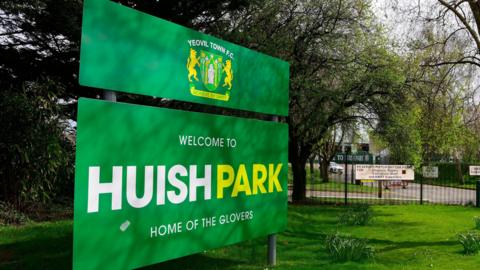 A green sign that says 'Welcome to Huish Park home of the Glovers' outside the gates of Huish Park