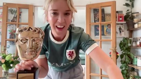 Lauren Evans wearing a green Welsh football shirt holding a golden BAFTA statue