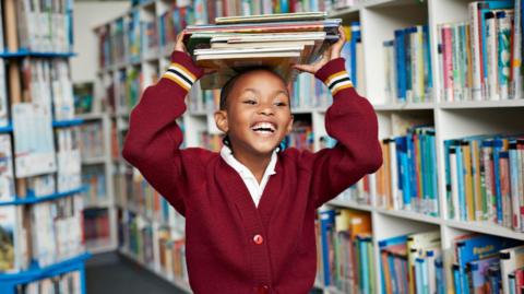 Smiling child with books on her head in the library 