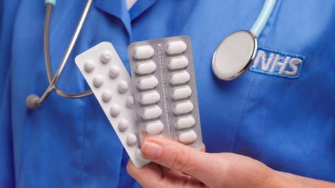 A stock photo of an NHS nurse holding medication.