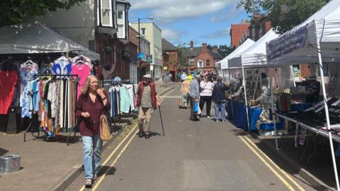 People walking down a narrow street with stalls on either side and buildings visible further down the street