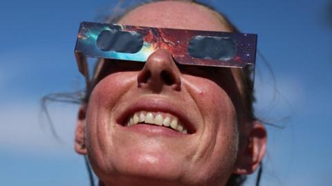 A woman looks up the sun while wearing a pair of special eclipse glasses to protect her eyes