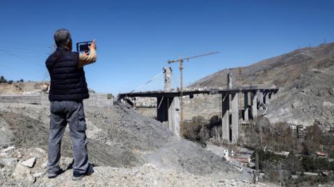 A man uses his phone to photograph the remains of the B1 bridge following a US air strike, in Karaj, northern Iran (3 April 2026)