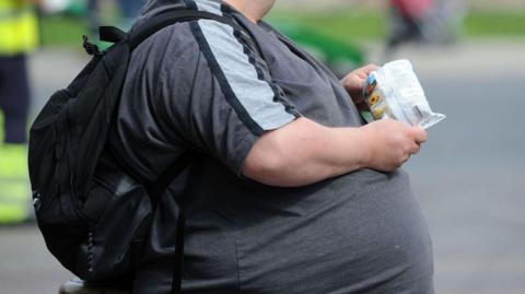  An overweight man with an obscured face eats crisps