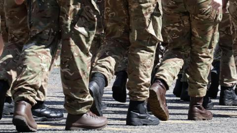 Soldiers' legs in uniform and boots walking from right to left.