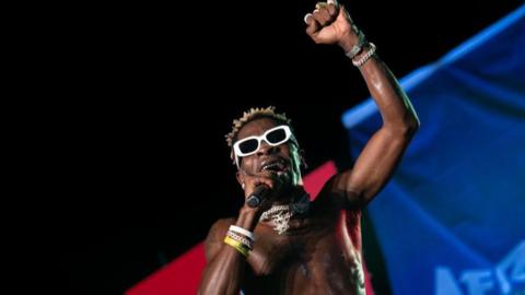 Shatta Wale performing on stage while shirtless and wearing white glasses 