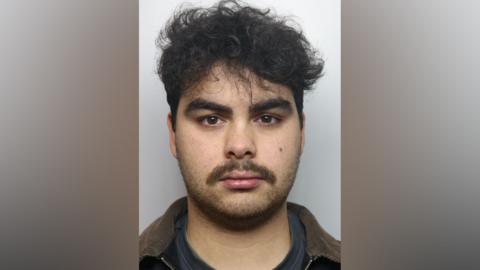 Kyran Smith mugshot. He has dark hair and dark stubble.