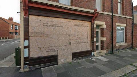 A Google street view screenshot of the takeaway unit on Coomassie Road, Blyth. The unit sits on a street corner and is boarded up. It is set within a residential area.