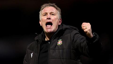 Phil Parkinson in a black Wrexham coat celebrates with a punch in the air