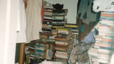 The bedroom of a person with hoarding disorder, stacked high with piles of books and clothes.