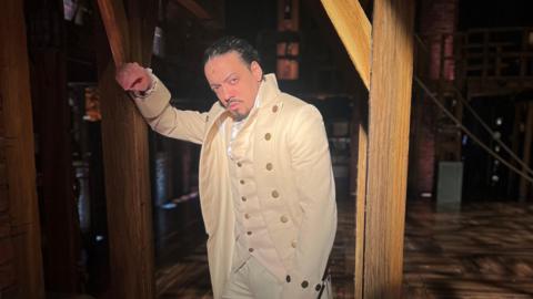 Levi Tyrell Johnson leans against the wooden stage in the wings at Hamilton