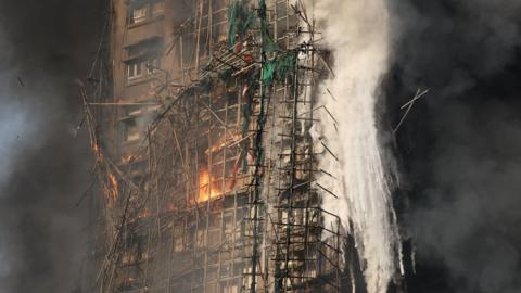 Destroyed tower with debris falling from it. The remains of the scaffolding - its frame - is still visible. Most of the fire on this part has been put out but there is still glows of it certain areas