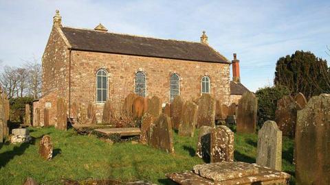 An old church in a graveyard with brick walls and big windows