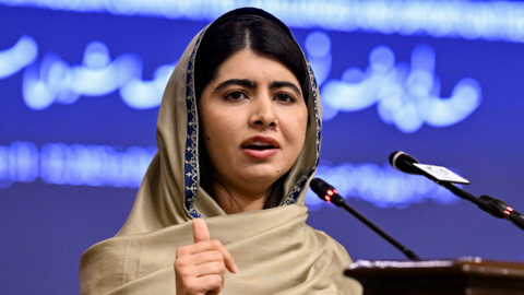 Malala speaking at a podium in front of a blue backdrop