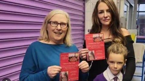 Heather Johnstone (centre) has long dark auburn hair and a black off the shoulder dress. Her mum Christine has blonde hair and is wearing a blue top. Her son Isaac has light brown hair and is wearing a purple and white school uniform.