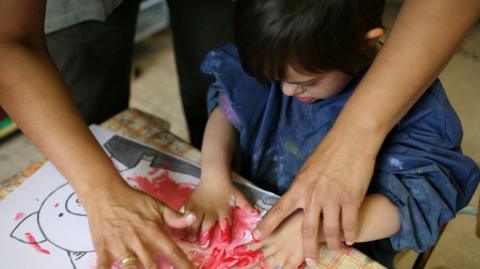 A child with Down's syndrome at school painting with their hands with an adult